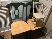 Two matching wood chairs painted green with natural wood seats, vintage style with curved backs and oval cutouts shown side by side