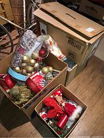 Boxes containing assorted Christmas decorations and boxes of Christmas lights, including gold, red, and silver ornaments, ribbons, and festive items.