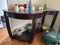 Console table showing beveled glass insert top, curved legs, and lower shelf. Dark wood finish visible. The table exhibits surface scratches.