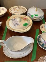 Photo showing four covered serving dishes with various floral and blue decorative patterns with one lid chipped, and a Royal Doulton gravy boat with saucer in foreground.