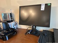 Dell 24 inch monitor on wooden surface with keyboard, USB cables around base, and other computer accessories nearby.