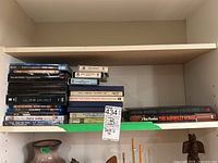 Shelf with assorted DVDs, 8-track tapes, reel to reel tapes, and books, stacked horizontally and vertically.