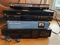 Top to bottom view of the stack: ElectroHome DVD player, Toshiba DVD/VCR combo, ElectroHome digital photo frame box, Zenith VHS video recorder.