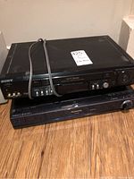 Photo showing a stacked Sony Hi-Fi Stereo VHS player on top of a Panasonic DVD player, both black with some dust and wear.
