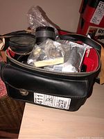 Top view of black zippered camera case filled with assorted camera accessories including lens and manuals.