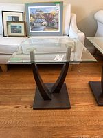 Front view of square glass top side table with two curved faux wood supports and square base.