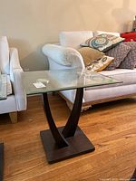 Side angle view of the glass top side table showing the glass and curved dark faux wood base.