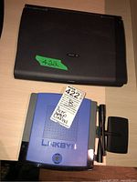 Black Acer laptop and blue Linksys wireless router with accessories including power adapter and two pens.
