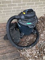 Mastervac black wet/dry shop vacuum unit with hose and collection bag sitting on wooden surface outdoors.
