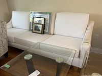 Full front view of the off-white three-seat sofa with coffee table in front and framed prints on cushions.