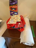 Assorted gift bags and wrapping paper placed on a wooden table including solid-colored bags and patterned wrapping paper sheets with white tissue paper roll.