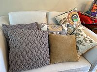 Five decorative pillows arranged on a white sofa showing colors, textures, and patterns.