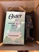 Boxed Oster electric skillet showing model and DiamondForce non-stick coating branding, also showing part of electric griddle handle beside box within shipping box.