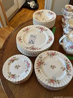Overview of all dinnerware pieces: stacks of dinner plates, side plates, bread plates, and bowls with floral motif