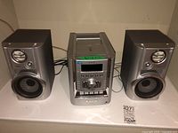 Full view of Sony CD sound system main unit and two speakers on a white surface showing front side with speaker cones and stereo controls.