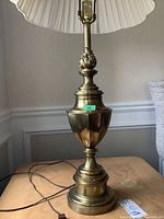 Full view of the vintage Stiffel metal table lamp on wood surface with pleated cream lampshade, showing ornate brass base with decorative details.