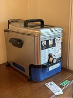 Side view of a silver and blue T-Fal deep fryer showing handle, lid and side vent.