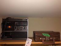 Overview of Aiwa radio cassette recorder and brown carrying case labeled 'Tapes' on shelf