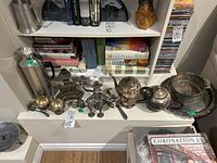 Image showing the full set of vintage silver plated items including coffee pot, teapot, salt and pepper shakers, candle holders, bowl holder, platter, and stainless steel carafe on a white shelf under books.