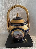Front view of blue and gold porcelain vase with handle on black base