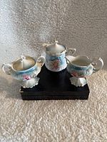 Image showing all three porcelain pieces on a textured fabric background with a black box beneath them.