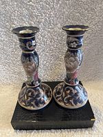 Pair of blue porcelain candle holders with floral designs placed on a black textured box, front view