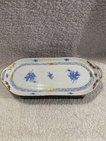 Porcelain platter displayed on a textured fabric background showing the top surface with blue floral design and gold trim.