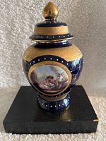 Front view of blue Limoges Design porcelain vase with lid showing painted romantic couple scene, gold and white dot accents.