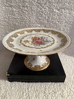 Porcelain plate displayed on matching pedestal stand showing entire set and gold decorative pattern
