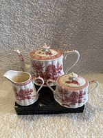 Red and white porcelain tea set on black stand against a textured backdrop.