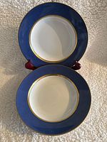 Two soup plates on display showing the blue and gold trim with white center bowl area.