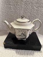 Front and side views of Sadler porcelain teapot showing hexagonal shape and detailed black and silver scenic floral designs.