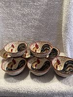 Photo showing 8 ceramic bowls stacked and angled to display the interior rooster design.