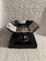 Side view of the dish on its stand showing cobalt blue color with white floral relief and gold accents.