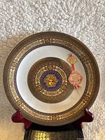 Full view of the decorative porcelain plate on a stand showing the Medusa head center with gold and blue accents and original brand stickers.