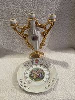 Photo showing the porcelain candle holder with two candle slots and the decorative plate with a Victorian scene centered, placed on a textured surface.
