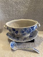 Front view of the blue and white ceramic tureen set including tureen, platter, and spoon arranged on light textured background.