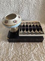 Sugar bowl and 6 teaspoons set placed on black box, showing side angle of sugar bowl and front of teaspoons in original box.