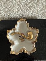 Front of vintage leaf-shaped porcelain decorative plate showing floral pattern and gold pipe detail.