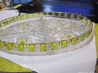 Close-up photo of round crystal serving dish with green trim and four compartments showing detailed cut patterns.