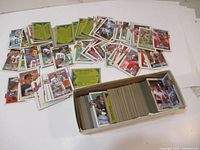 Wide view of a large number of 1988 Topps football cards spread out on a surface with a box holding many more cards arranged.