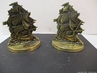 Both brass ship bookends shown upright on a black surface, displaying detailed ship design and brass base.