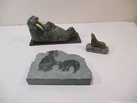 Wide view showing all three soapstone items: walrus figure, seal figure on base, and carved plaque.