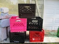 Five plastic storage crates stacked outside near outdoor wall and garage door.