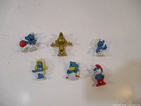 Overview of six Smurf figurines including a golden Smurf and five classic blue Smurfs with various accessories and poses.