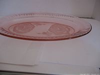 Side angled view showing the pink oval glass platter with embossed floral designs and textured edge.