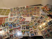 Wide angled photo showing a spread of numerous baseball cards laid out on a white surface, with many in protective sleeves and assorted teams represented