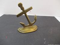 Solid brass anchor paperweight or bookend shown from an angle, placed on a flat black surface with a white background.