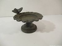 Side view of small cast iron bird bath showing butterfly detail and scalloped rim.