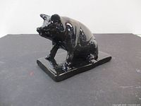 Front view of the shiny black cast iron pig figurine on its base.